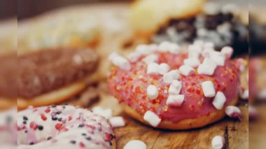 Çikolata, marşmelov ve retro pişirme tepsisindeki şekerli çörekler. Donutlar doğal çikolatayla süslenmiş bir kağıdın üzerinde. Makro ve kaydırma atışı. Çeşitli renkli çörekler. Çikolata, pembe, mavi çörekler