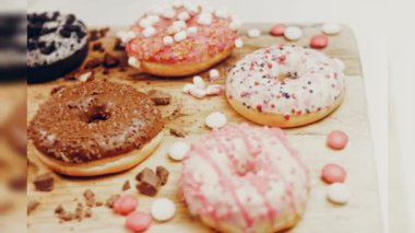 Çikolata, marşmelov ve retro pişirme tepsisindeki şekerli çörekler. Donutlar doğal çikolatayla süslenmiş bir kağıdın üzerinde. Makro ve kaydırma atışı. Çeşitli renkli çörekler. Çikolata, pembe, mavi çörekler