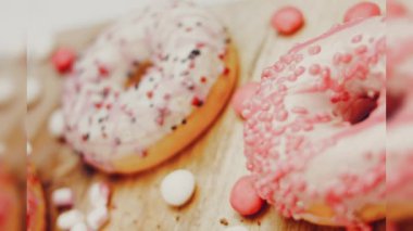 Çikolata, marşmelov ve retro pişirme tepsisindeki şekerli çörekler. Donutlar doğal çikolatayla süslenmiş bir kağıdın üzerinde. Makro ve kaydırma atışı. Çeşitli renkli çörekler. Çikolata, pembe, mavi çörekler