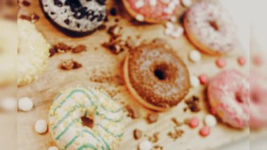 Çikolata, marşmelov ve retro pişirme tepsisindeki şekerli çörekler. Donutlar doğal çikolatayla süslenmiş bir kağıdın üzerinde. Makro ve kaydırma atışı. Çeşitli renkli çörekler. Çikolata, pembe, mavi çörekler