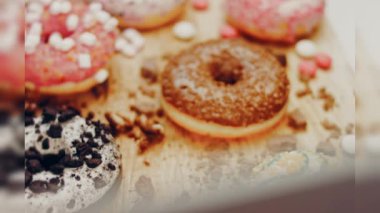 Çikolata, marşmelov ve retro pişirme tepsisindeki şekerli çörekler. Donutlar doğal çikolatayla süslenmiş bir kağıdın üzerinde. Makro ve kaydırma atışı. Çeşitli renkli çörekler. Çikolata, pembe, mavi çörekler