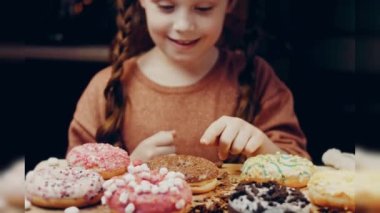 Kız hediyeler arasından seçiyor, parmağını işaret ediyor. Çikolata, marşmelov ve retro pişirme tepsisindeki şekerli çörekler. Donutlar doğal çikolatayla süslenmiş bir kağıdın üzerinde. Makro ve kaydırıcı