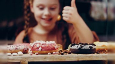 Kız hediyeler arasından seçiyor, parmağını işaret ediyor. Çikolata, marşmelov ve retro pişirme tepsisindeki şekerli çörekler. Donutlar doğal çikolatayla süslenmiş bir kağıdın üzerinde. Makro ve kaydırıcı