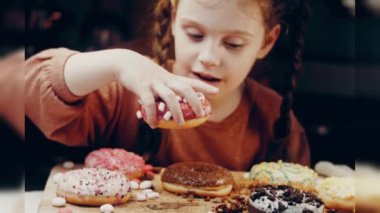 Kız hediyeler arasından seçiyor, parmağını işaret ediyor. Çikolata, marşmelov ve retro pişirme tepsisindeki şekerli çörekler. Donutlar doğal çikolatayla süslenmiş bir kağıdın üzerinde. Makro ve kaydırıcı