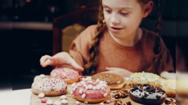 Kız hediyeler arasından seçiyor, parmağını işaret ediyor. Çikolata, marşmelov ve retro pişirme tepsisindeki şekerli çörekler. Donutlar doğal çikolatayla süslenmiş bir kağıdın üzerinde. Makro ve kaydırıcı