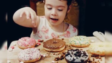 Kız hediyeler arasından seçiyor, parmağını işaret ediyor. Çikolata, marşmelov ve retro pişirme tepsisindeki şekerli çörekler. Donutlar doğal çikolatayla süslenmiş bir kağıdın üzerinde. Makro ve kaydırıcı