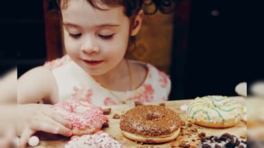 Kız hediyeler arasından seçiyor, parmağını işaret ediyor. Çikolata, marşmelov ve retro pişirme tepsisindeki şekerli çörekler. Donutlar doğal çikolatayla süslenmiş bir kağıdın üzerinde. Makro ve kaydırıcı