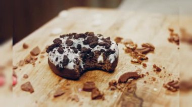 Donut 'ın ağız şeklinde bir ısırığı var. Oeo bisküvileriyle süslenmiş çikolatalı çörekler. Donutlar doğal çikolatayla süslenmiş bir kağıdın üzerinde. Makro ve kaydırma atışı. Fırın ve gıda konsepti