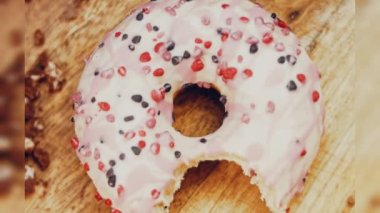 Pembe kremayla süslenmiş pembe çörekler. Çörekler şekerle süslenmiş bir kağıt parçasının üzerinde. Makro ve kaydırma atışı. Şekerler ağır çekimde hareket ediyor. Fırın ve yemek konsepti. Çeşitli renkli çörekler.