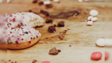 Pembe kremayla süslenmiş pembe çörekler. Çörekler şekerle süslenmiş bir kağıt parçasının üzerinde. Makro ve kaydırma atışı. Şekerler ağır çekimde hareket ediyor. Fırın ve yemek konsepti. Çeşitli renkli çörekler.