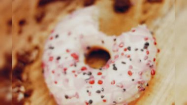 Pembe kremayla süslenmiş pembe çörekler. Çörekler şekerle süslenmiş bir kağıt parçasının üzerinde. Makro ve kaydırma atışı. Şekerler ağır çekimde hareket ediyor. Fırın ve yemek konsepti. Çeşitli renkli çörekler.