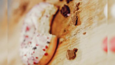 Pembe kremayla süslenmiş pembe çörekler. Çörekler şekerle süslenmiş bir kağıt parçasının üzerinde. Makro ve kaydırma atışı. Şekerler ağır çekimde hareket ediyor. Fırın ve yemek konsepti. Çeşitli renkli çörekler.