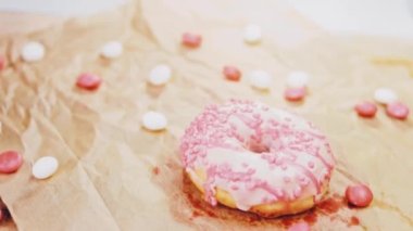 Pembe kremayla süslenmiş pembe çörekler. Çörekler şekerle süslenmiş bir kağıt parçasının üzerinde. Makro ve kaydırma atışı. Şekerler ağır çekimde hareket ediyor. Fırın ve yemek konsepti. Çeşitli renkli çörekler.