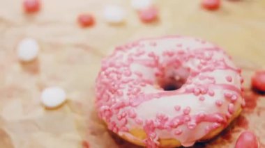 Pembe kremayla süslenmiş pembe çörekler. Çörekler şekerle süslenmiş bir kağıt parçasının üzerinde. Makro ve kaydırma atışı. Şekerler ağır çekimde hareket ediyor. Fırın ve yemek konsepti. Çeşitli renkli çörekler.