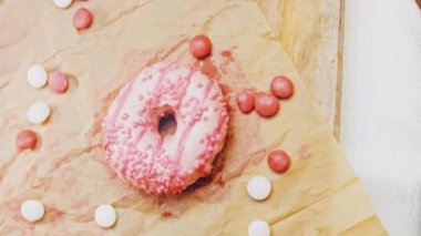 Pembe kremayla süslenmiş pembe çörekler. Çörekler şekerle süslenmiş bir kağıt parçasının üzerinde. Makro ve kaydırma atışı. Şekerler ağır çekimde hareket ediyor. Fırın ve yemek konsepti. Çeşitli renkli çörekler.