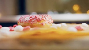 Pembe kremayla süslenmiş pembe çörekler. Çörekler şekerle süslenmiş bir kağıt parçasının üzerinde. Makro ve kaydırma atışı. Şekerler ağır çekimde hareket ediyor. Fırın ve yemek konsepti. Çeşitli renkli çörekler.