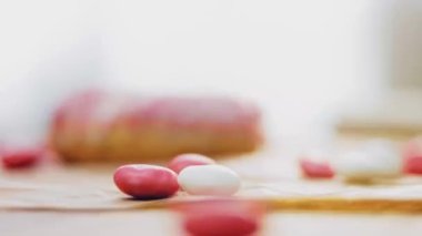 Pembe kremayla süslenmiş pembe çörekler. Çörekler şekerle süslenmiş bir kağıt parçasının üzerinde. Makro ve kaydırma atışı. Şekerler ağır çekimde hareket ediyor. Fırın ve yemek konsepti. Çeşitli renkli çörekler.