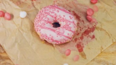 Pembe kremayla süslenmiş pembe çörekler. Çörekler şekerle süslenmiş bir kağıt parçasının üzerinde. Makro ve kaydırma atışı. Şekerler ağır çekimde hareket ediyor. Fırın ve yemek konsepti. Çeşitli renkli çörekler.