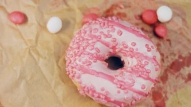 Pembe kremayla süslenmiş pembe çörekler. Çörekler şekerle süslenmiş bir kağıt parçasının üzerinde. Makro ve kaydırma atışı. Şekerler ağır çekimde hareket ediyor. Fırın ve yemek konsepti. Çeşitli renkli çörekler.