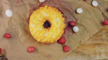 Sarı kremayla süslenmiş pembe çörekler. Çörekler şekerle süslenmiş bir kağıt parçasının üzerinde. Makro ve kaydırma atışı. Şekerler ağır çekimde hareket eder..