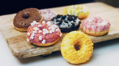 Çikolata, marşmelov ve retro pişirme tepsisindeki şekerli çörekler. Donutlar doğal çikolatayla süslenmiş bir kağıdın üzerinde. Makro ve kaydırma atışı. Çeşitli renkli çörekler. Çikolata, pembe, mavi çörekler