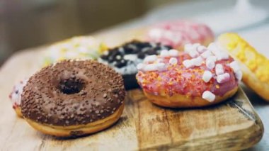 Çikolata, marşmelov ve retro pişirme tepsisindeki şekerli çörekler. Donutlar doğal çikolatayla süslenmiş bir kağıdın üzerinde. Makro ve kaydırma atışı. Çeşitli renkli çörekler. Çikolata, pembe, mavi çörekler