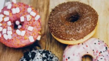 Çikolata, marşmelov ve retro pişirme tepsisindeki şekerli çörekler. Donutlar doğal çikolatayla süslenmiş bir kağıdın üzerinde. Makro ve kaydırma atışı. Çeşitli renkli çörekler. Çikolata, pembe, mavi çörekler