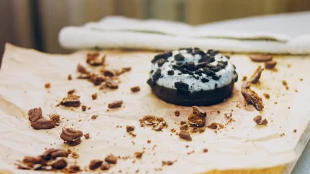 チョコレートドーナツはオレオビスケットのピースで飾られています ドーナツは自然チョコレートで飾られた紙の上にあります マクロとスライダーの撮影 パン屋と食のコンセプト 色とりどりのドーナツ チョコレート — ストック動画