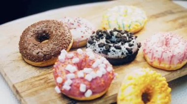 Çikolata, marşmelov ve retro pişirme tepsisindeki şekerli çörekler. Donutlar doğal çikolatayla süslenmiş bir kağıdın üzerinde. Makro ve kaydırma atışı. Çeşitli renkli çörekler. Çikolata, pembe, mavi çörekler