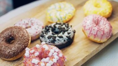 Çikolata, marşmelov ve retro pişirme tepsisindeki şekerli çörekler. Donutlar doğal çikolatayla süslenmiş bir kağıdın üzerinde. Makro ve kaydırma atışı. Çeşitli renkli çörekler. Çikolata, pembe, mavi çörekler