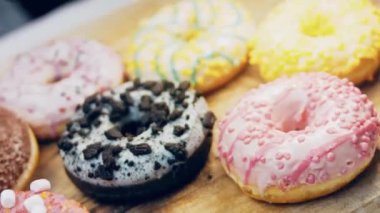 Çikolata, marşmelov ve retro pişirme tepsisindeki şekerli çörekler. Donutlar doğal çikolatayla süslenmiş bir kağıdın üzerinde. Makro ve kaydırma atışı. Çeşitli renkli çörekler. Çikolata, pembe, mavi çörekler