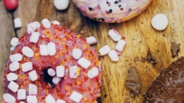 Çikolata, marşmelov ve retro pişirme tepsisindeki şekerli çörekler. Donutlar doğal çikolatayla süslenmiş bir kağıdın üzerinde. Makro ve kaydırma atışı. Çeşitli renkli çörekler. Çikolata, pembe, mavi çörekler