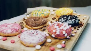 Çikolata, marşmelov ve retro pişirme tepsisindeki şekerli çörekler. Donutlar doğal çikolatayla süslenmiş bir kağıdın üzerinde. Makro ve kaydırma atışı. Çeşitli renkli çörekler. Çikolata, pembe, mavi çörekler