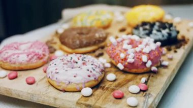 Çikolata, marşmelov ve retro pişirme tepsisindeki şekerli çörekler. Donutlar doğal çikolatayla süslenmiş bir kağıdın üzerinde. Makro ve kaydırma atışı. Çeşitli renkli çörekler. Çikolata, pembe, mavi çörekler