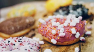 Çikolata, marşmelov ve retro pişirme tepsisindeki şekerli çörekler. Donutlar doğal çikolatayla süslenmiş bir kağıdın üzerinde. Makro ve kaydırma atışı. Çeşitli renkli çörekler. Çikolata, pembe, mavi çörekler