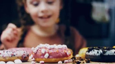 Kız hediyeler arasından seçiyor, parmağını işaret ediyor. Çikolata, marşmelov ve retro pişirme tepsisindeki şekerli çörekler. Donutlar doğal çikolatayla süslenmiş bir kağıdın üzerinde. Makro ve kaydırıcı