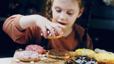 Kız hediyeler arasından seçiyor, parmağını işaret ediyor. Çikolata, marşmelov ve retro pişirme tepsisindeki şekerli çörekler. Donutlar doğal çikolatayla süslenmiş bir kağıdın üzerinde. Makro ve kaydırıcı