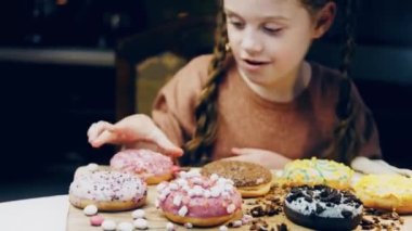 Kız hediyeler arasından seçiyor, parmağını işaret ediyor. Çikolata, marşmelov ve retro pişirme tepsisindeki şekerli çörekler. Donutlar doğal çikolatayla süslenmiş bir kağıdın üzerinde. Makro ve kaydırıcı