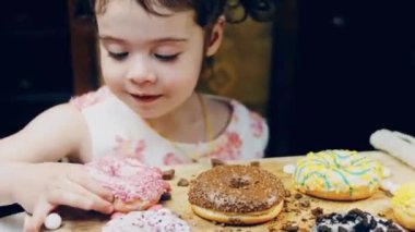 Kız donut yiyor. Çikolata, marşmelov ve retro pişirme tepsisindeki şekerli çörekler. Donutlar doğal çikolatayla süslenmiş bir kağıdın üzerinde. Makro ve kaydırma atışı. Çeşitli renkli çörekler.