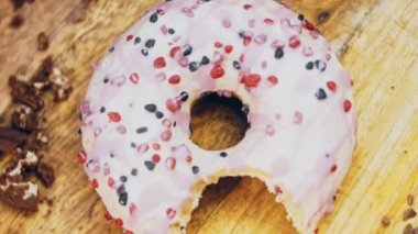 Pembe kremayla süslenmiş pembe çörekler. Çörekler şekerle süslenmiş bir kağıt parçasının üzerinde. Makro ve kaydırma atışı. Şekerler ağır çekimde hareket ediyor. Fırın ve yemek konsepti. Çeşitli renkli çörekler.