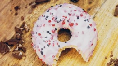 Pembe kremayla süslenmiş pembe çörekler. Çörekler şekerle süslenmiş bir kağıt parçasının üzerinde. Makro ve kaydırma atışı. Şekerler ağır çekimde hareket ediyor. Fırın ve yemek konsepti. Çeşitli renkli çörekler.