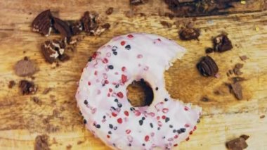 Pembe kremayla süslenmiş pembe çörekler. Çörekler şekerle süslenmiş bir kağıt parçasının üzerinde. Makro ve kaydırma atışı. Şekerler ağır çekimde hareket ediyor. Fırın ve yemek konsepti. Çeşitli renkli çörekler.