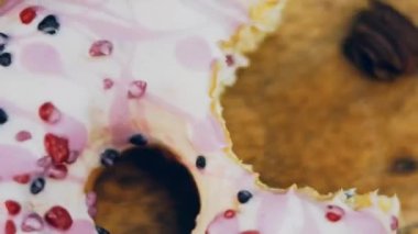Pembe kremayla süslenmiş pembe çörekler. Çörekler şekerle süslenmiş bir kağıt parçasının üzerinde. Makro ve kaydırma atışı. Şekerler ağır çekimde hareket ediyor. Fırın ve yemek konsepti. Çeşitli renkli çörekler.