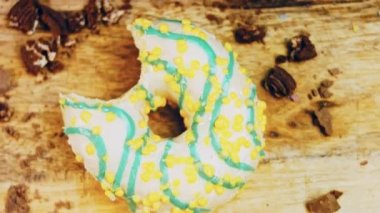 Donut 'ın ağız şeklinde bir ısırığı var. Mavi kremayla süslenmiş sarı çörekler. Çörekler şekerle süslenmiş bir kağıt parçasının üzerinde. Makro ve kaydırma atışı. Makro ve kaydırma atışı. Şekerler içeri giriyor.