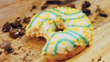 Donut 'ın ağız şeklinde bir ısırığı var. Mavi kremayla süslenmiş sarı çörekler. Çörekler şekerle süslenmiş bir kağıt parçasının üzerinde. Makro ve kaydırma atışı. Makro ve kaydırma atışı. Şekerler içeri giriyor.