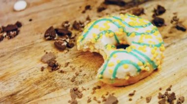 Donut 'ın ağız şeklinde bir ısırığı var. Mavi kremayla süslenmiş sarı çörekler. Çörekler şekerle süslenmiş bir kağıt parçasının üzerinde. Makro ve kaydırma atışı. Makro ve kaydırma atışı. Şekerler içeri giriyor.