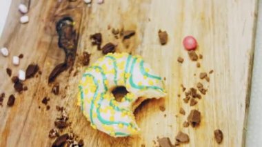 Donut 'ın ağız şeklinde bir ısırığı var. Mavi kremayla süslenmiş sarı çörekler. Çörekler şekerle süslenmiş bir kağıt parçasının üzerinde. Makro ve kaydırma atışı. Makro ve kaydırma atışı. Şekerler içeri giriyor.