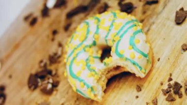 Donut 'ın ağız şeklinde bir ısırığı var. Mavi kremayla süslenmiş sarı çörekler. Çörekler şekerle süslenmiş bir kağıt parçasının üzerinde. Makro ve kaydırma atışı. Makro ve kaydırma atışı. Şekerler içeri giriyor.