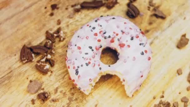 ピンクのドーナツはピンクのアイシングで飾られています ドーナツはキャンディで装飾された紙の上にあります マクロとスライダーの撮影 キャンディーはゆっくりと動きます パン屋と食のコンセプト カラフルなドーナツ — ストック動画