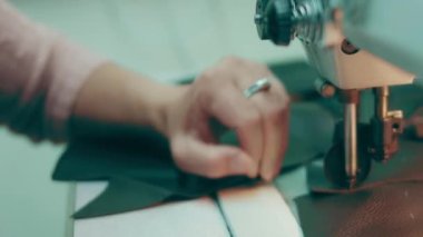 Deri atölyesinde dikiş makinesi çalışıyor. Elleri ayakkabı için deri detaylar üzerinde çalışıyor. Ayakkabı fabrikasında dikiş makinesiyle kadın eli makro çekim..